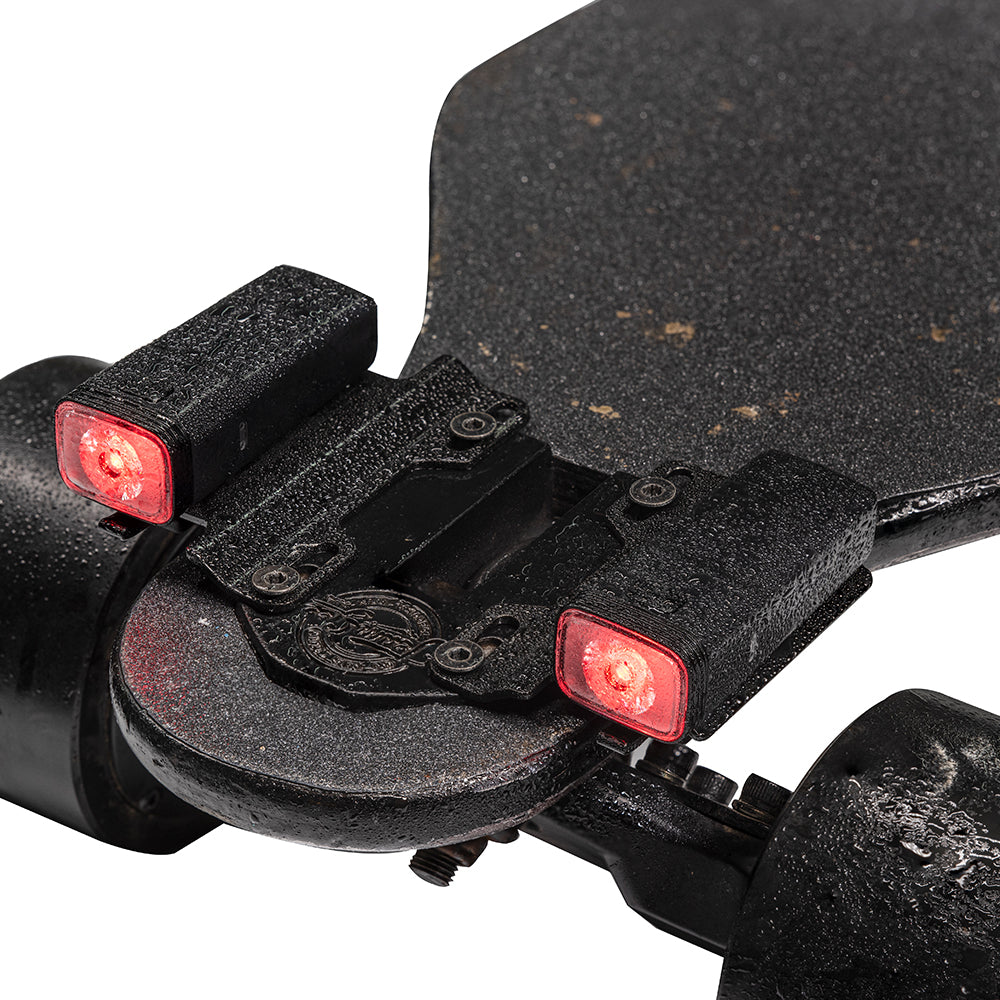 Close-up of a skateboard with red lights attached to the trucks on a white background