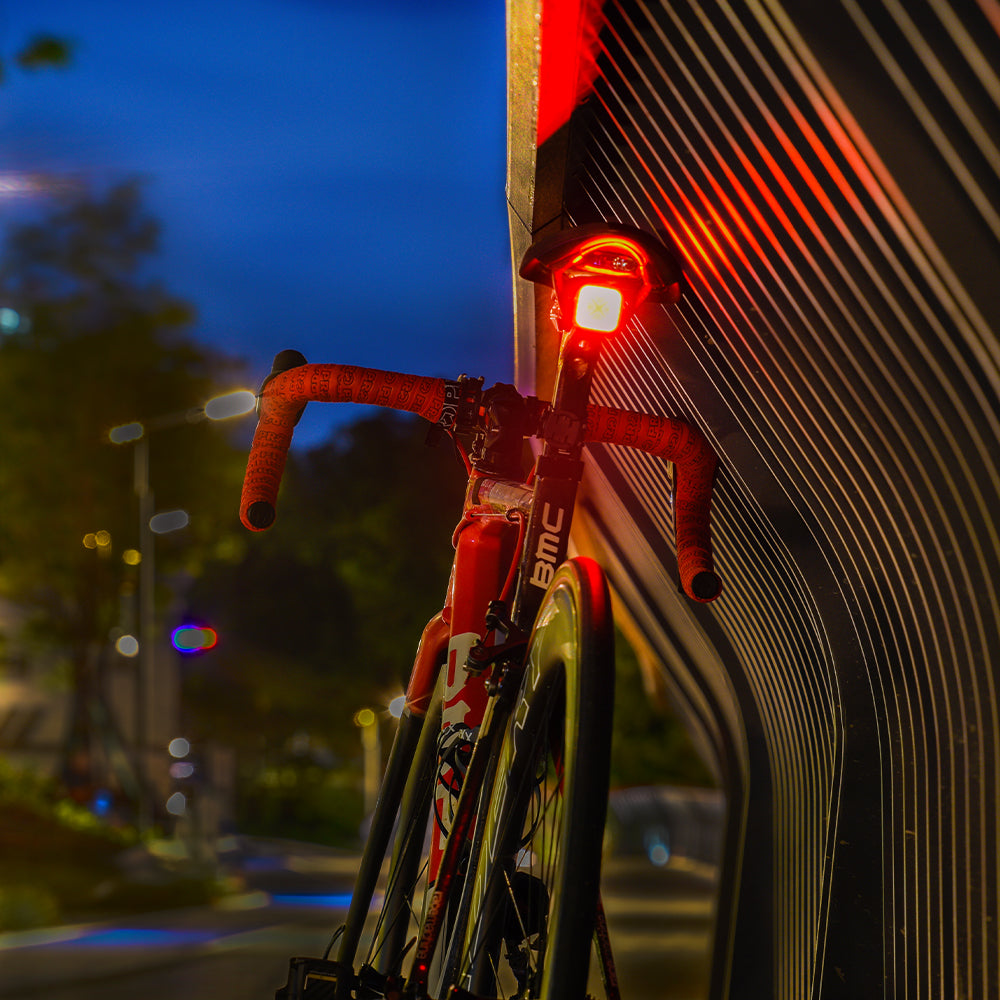 Bicycle with a red light attached to its handlebar, parked against a wall at night.