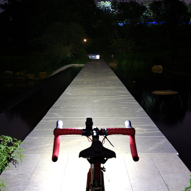 Bicycle handlebars with red grips on a wooden boardwalk at night.